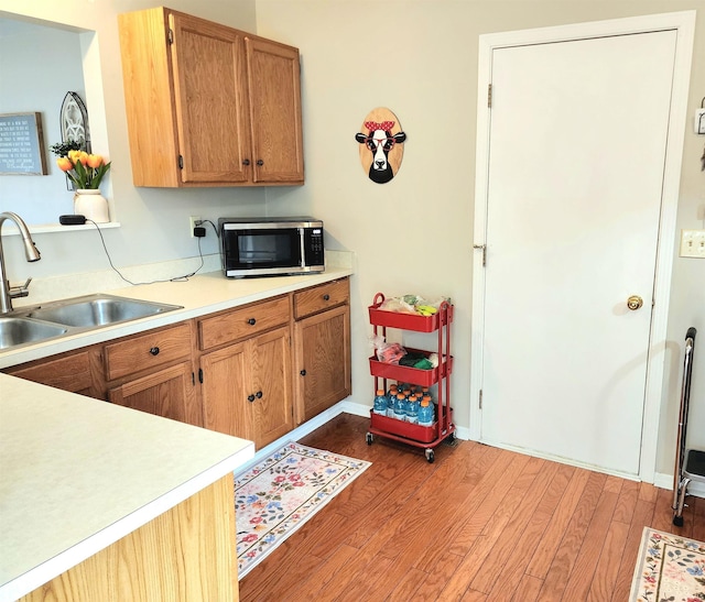 kitchen featuring a sink, stainless steel microwave, light wood-style floors, and light countertops