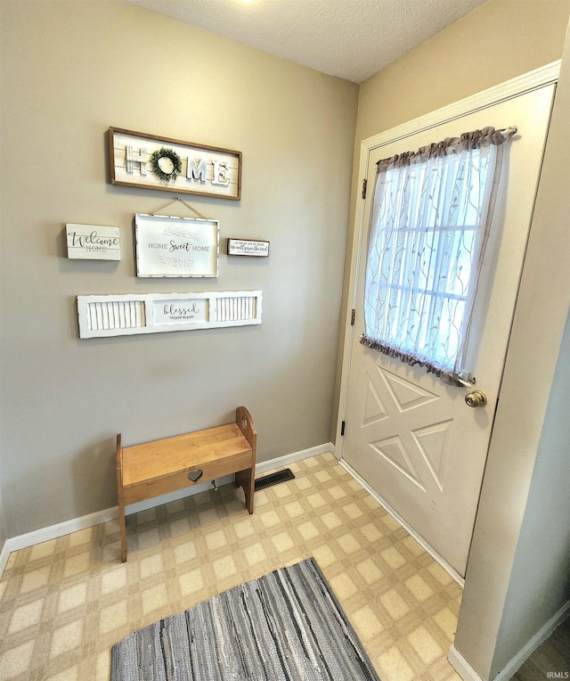 entryway featuring a textured ceiling, light floors, visible vents, and baseboards