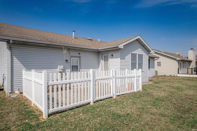 rear view of property with a lawn, roof with shingles, and fence