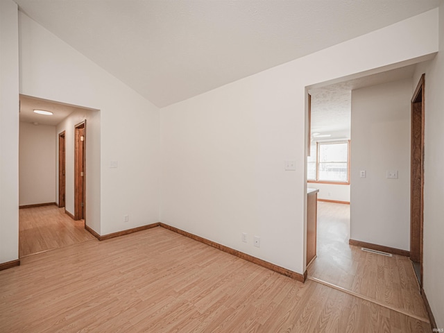 unfurnished room with light wood-style flooring, baseboards, and vaulted ceiling