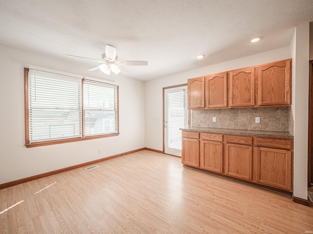 kitchen featuring tasteful backsplash, visible vents, baseboards, light wood-type flooring, and a ceiling fan