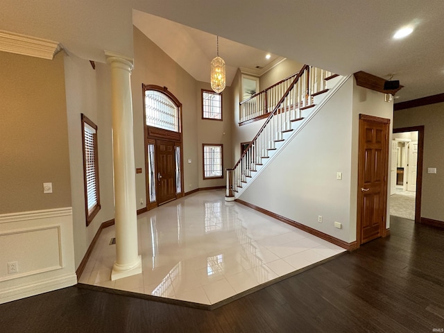 entryway featuring decorative columns, wood finished floors, ornamental molding, and stairs