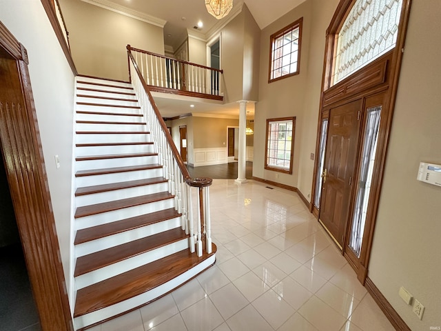 foyer featuring stairs, crown molding, a high ceiling, and decorative columns