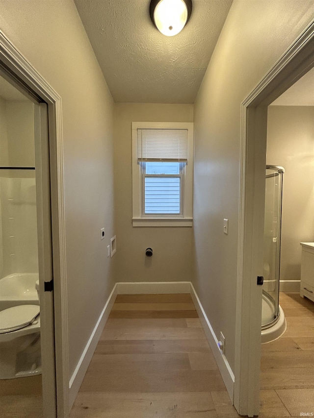 hall featuring light wood-type flooring, baseboards, and a textured ceiling