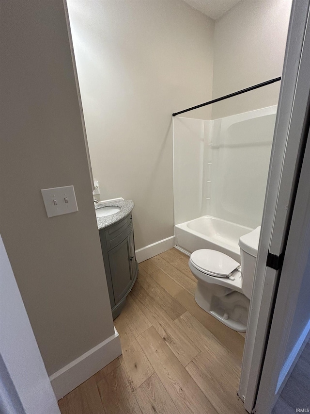 bathroom featuring vanity, wood finished floors, baseboards, bathing tub / shower combination, and toilet