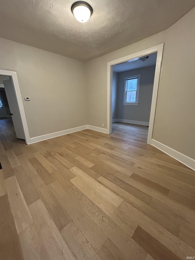 spare room featuring a textured ceiling, light wood-type flooring, and baseboards