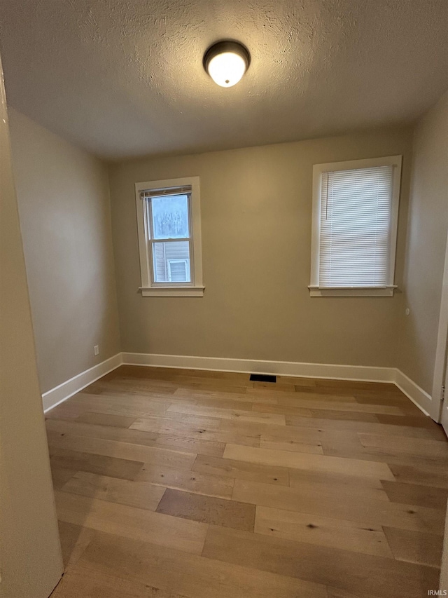 empty room with visible vents, a textured ceiling, baseboards, and wood finished floors