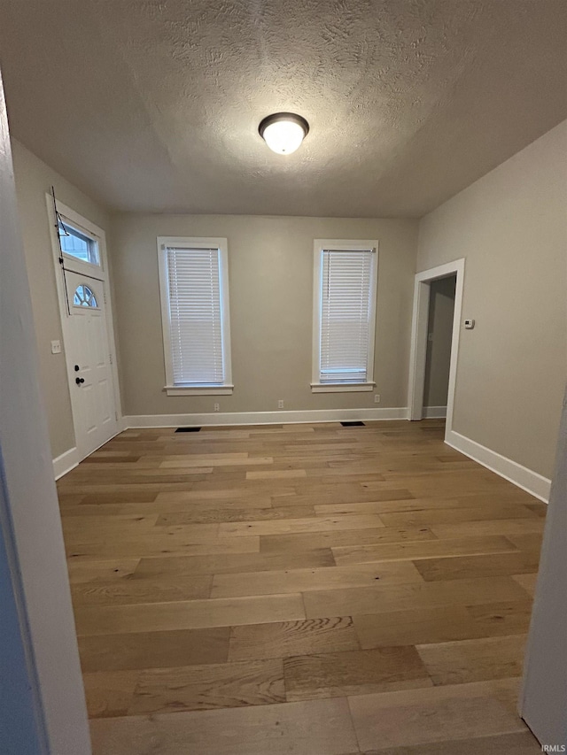 empty room featuring visible vents, baseboards, light wood-type flooring, and a textured ceiling