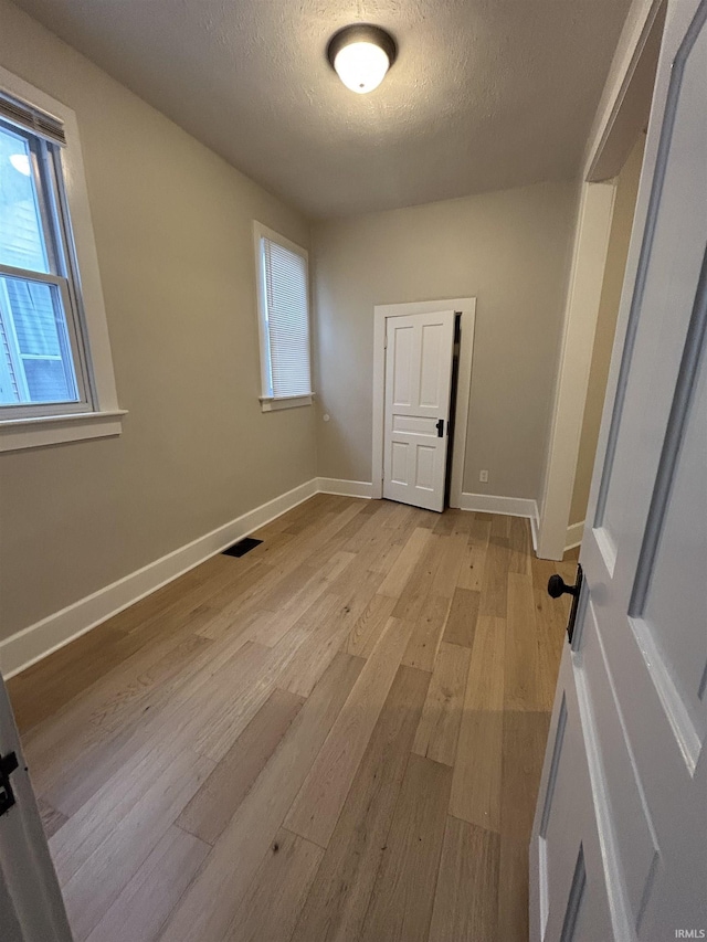 unfurnished room featuring visible vents, a textured ceiling, baseboards, and light wood-style floors