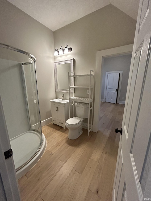 bathroom with wood finished floors, toilet, lofted ceiling, and a stall shower