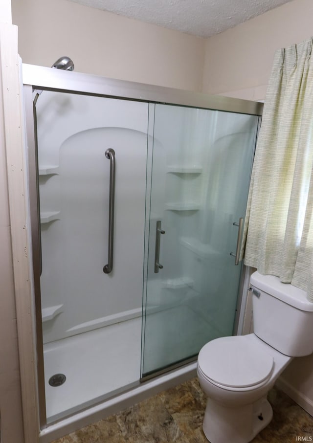 bathroom featuring toilet, a stall shower, and a textured ceiling