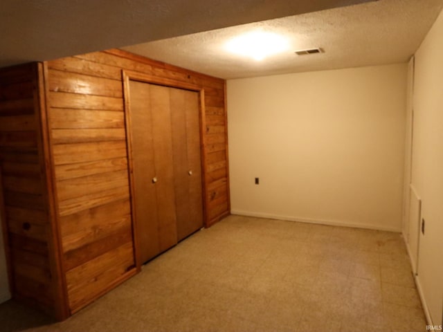unfurnished bedroom featuring light floors, visible vents, a closet, wood walls, and a textured ceiling