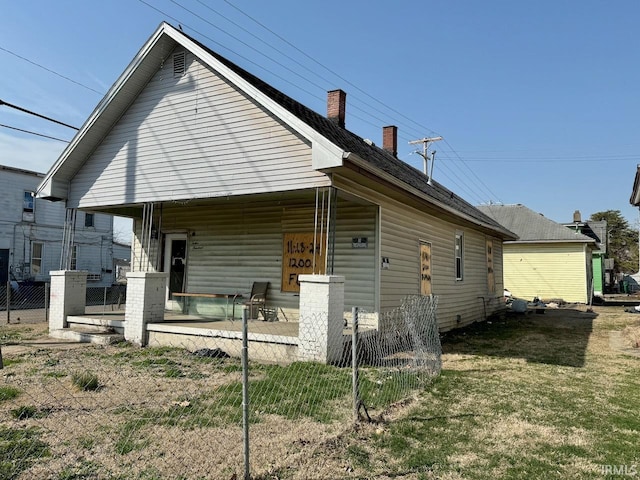back of house with a porch, a chimney, and fence