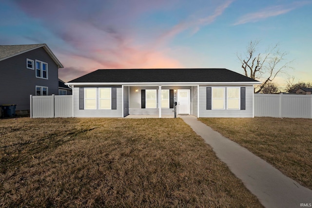 back of house at dusk with roof with shingles, a yard, and fence