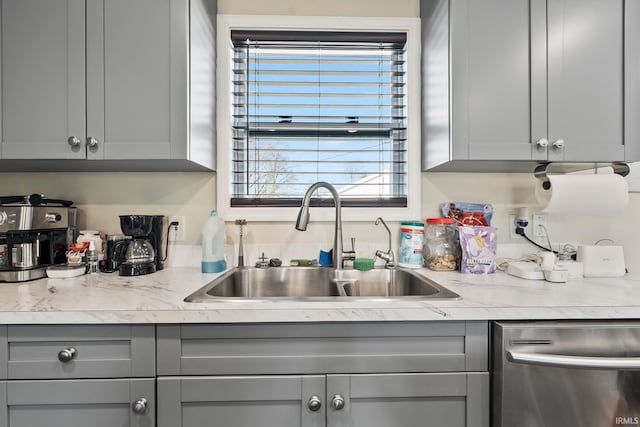 kitchen with a sink, gray cabinetry, light countertops, and stainless steel dishwasher