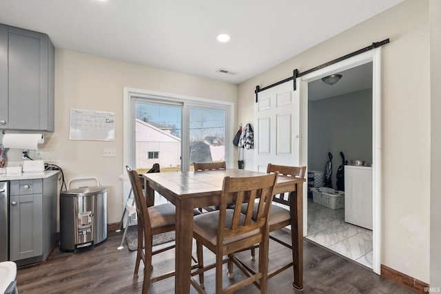 dining area with a barn door, dark wood-style floors, visible vents, and baseboards