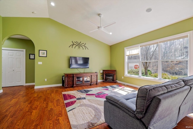 living room with a ceiling fan, wood finished floors, arched walkways, baseboards, and vaulted ceiling