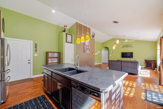 kitchen featuring wood finished floors, arched walkways, a sink, stainless steel appliances, and vaulted ceiling