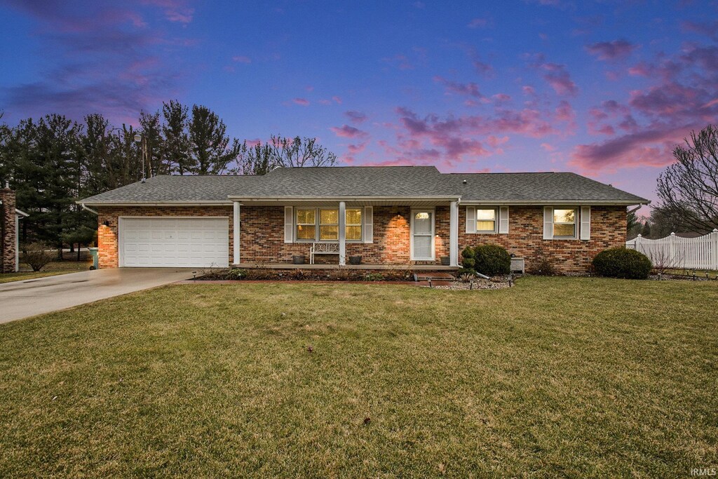 ranch-style home featuring brick siding, an attached garage, fence, a front yard, and driveway