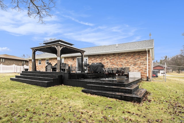 rear view of house featuring a lawn, a deck, fence, a gazebo, and brick siding