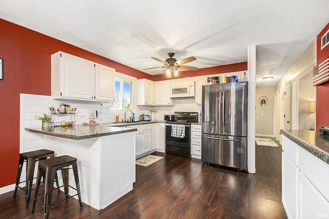 kitchen with dark wood finished floors, a peninsula, dark countertops, and appliances with stainless steel finishes