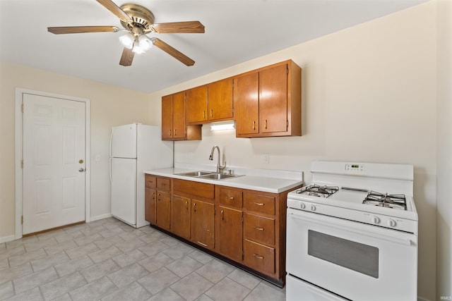 kitchen featuring light countertops, brown cabinetry, white appliances, a ceiling fan, and a sink