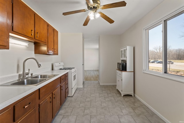 kitchen featuring stainless steel microwave, light countertops, white range with gas cooktop, brown cabinetry, and a sink