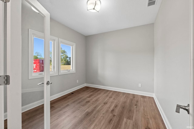 empty room featuring wood finished floors, baseboards, and visible vents