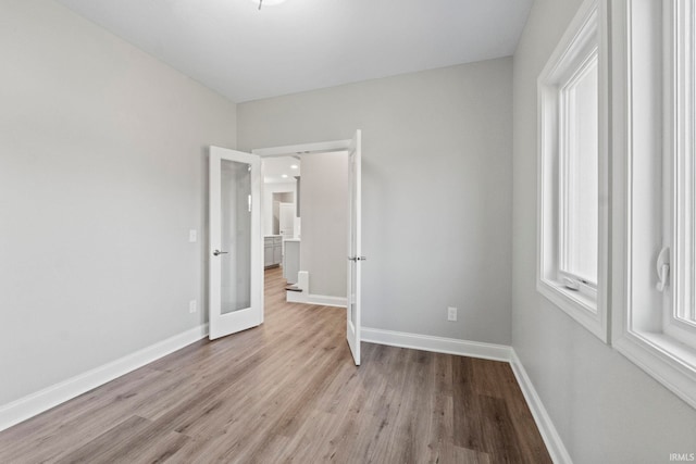 unfurnished bedroom with light wood-style flooring, french doors, and baseboards