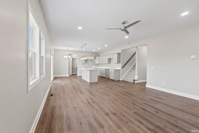 unfurnished living room with a sink, baseboards, light wood finished floors, and ceiling fan with notable chandelier