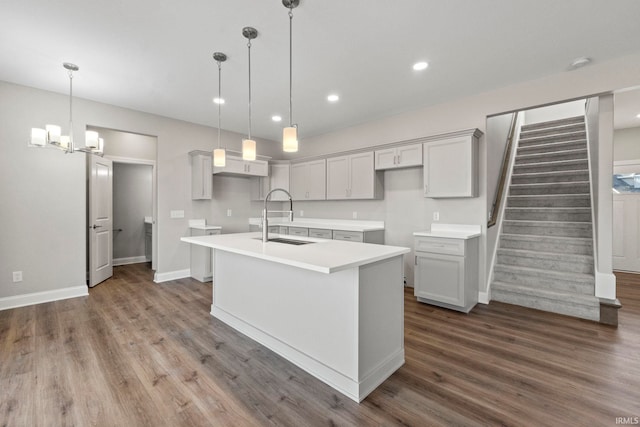 kitchen with hanging light fixtures, a kitchen island with sink, dark wood-style flooring, and a sink