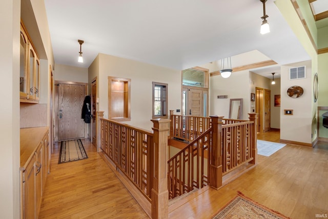 hallway featuring light wood-style flooring, an upstairs landing, visible vents, and baseboards