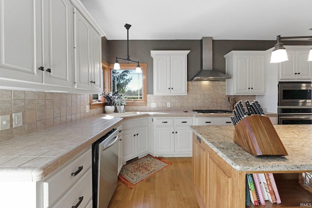kitchen with decorative backsplash, stainless steel appliances, light wood-style floors, white cabinetry, and wall chimney exhaust hood