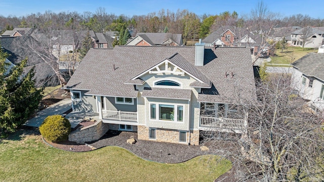 exterior space featuring stone siding, a yard, a residential view, roof with shingles, and a chimney
