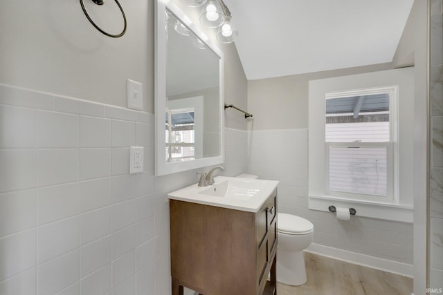 bathroom with vanity, wood finished floors, a wainscoted wall, tile walls, and toilet