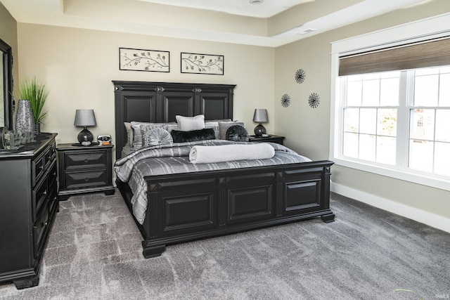 carpeted bedroom with a raised ceiling and baseboards