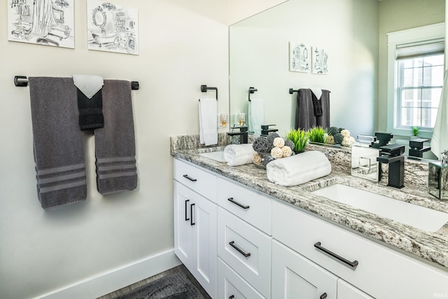 full bath with double vanity, baseboards, and a sink