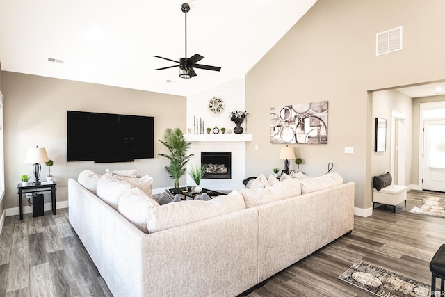 living room featuring dark wood-style floors, visible vents, a fireplace, and a ceiling fan
