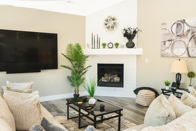living room with lofted ceiling, wood finished floors, baseboards, and a large fireplace