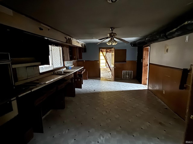 kitchen with a wealth of natural light, a wainscoted wall, wood walls, and a ceiling fan
