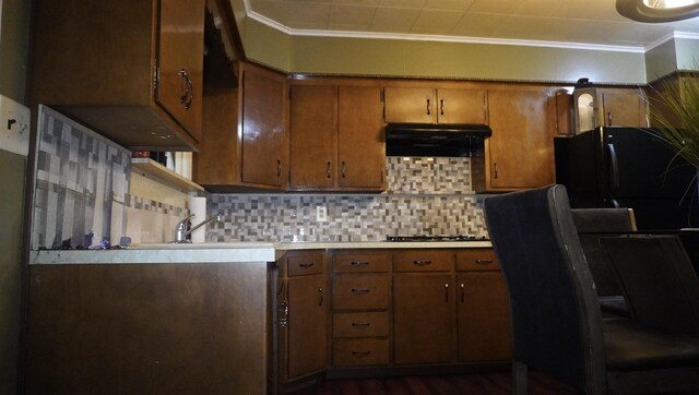 kitchen with decorative backsplash, light countertops, black appliances, under cabinet range hood, and crown molding