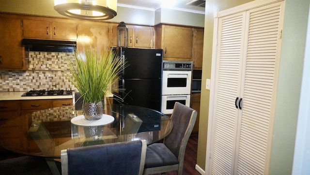 kitchen featuring brown cabinets, under cabinet range hood, tasteful backsplash, freestanding refrigerator, and double oven