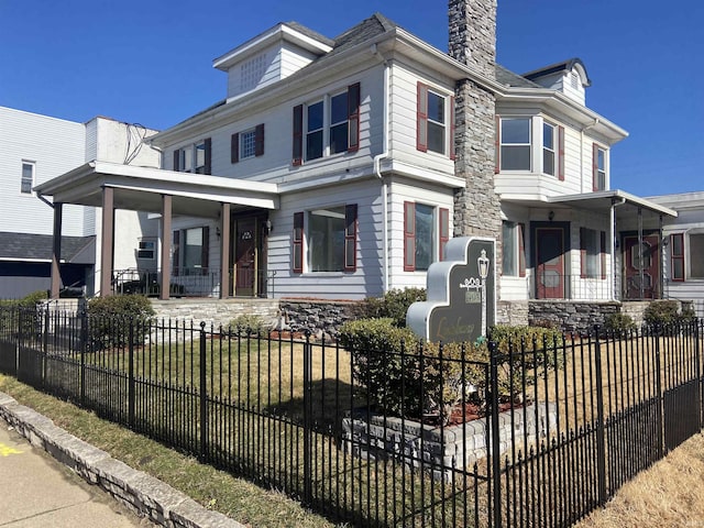 traditional style home with a chimney, a fenced front yard, and covered porch
