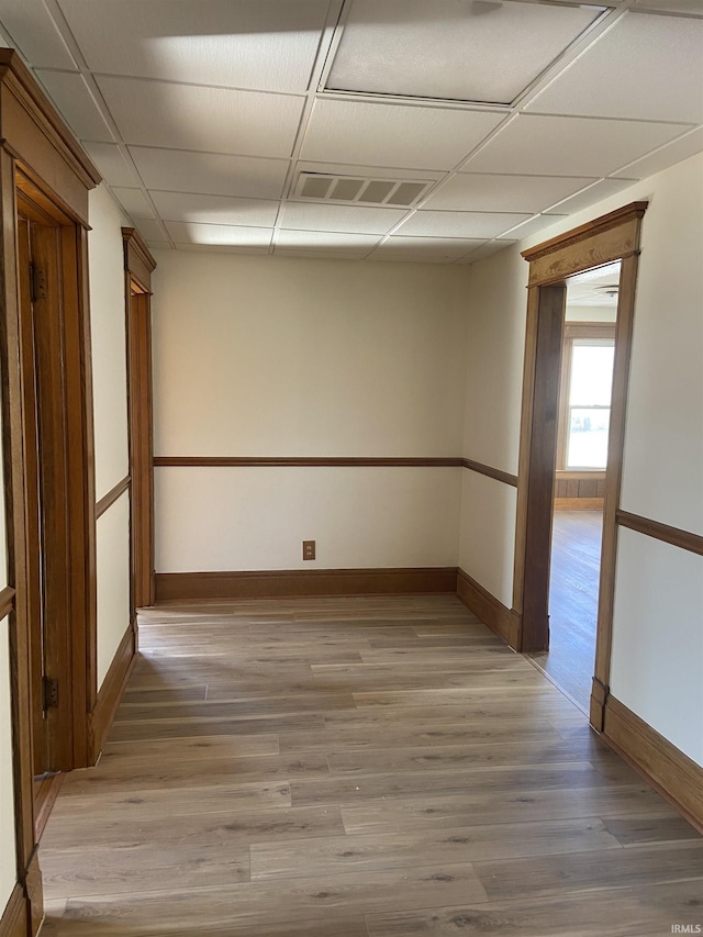 spare room featuring baseboards, visible vents, a paneled ceiling, and light wood-style floors