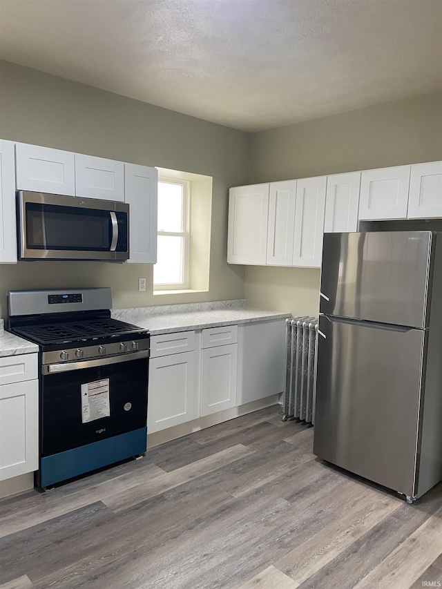 kitchen featuring light countertops, white cabinets, radiator, and stainless steel appliances