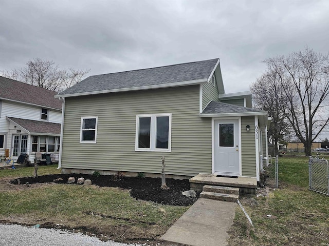 view of front of house featuring a shingled roof, a front yard, and fence