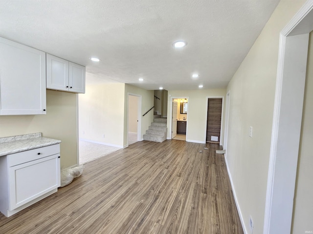 unfurnished living room with light wood-type flooring, baseboards, recessed lighting, and stairs