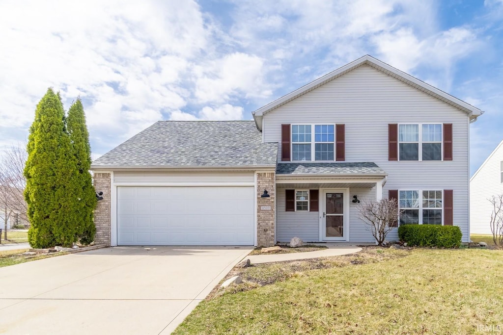 traditional home featuring concrete driveway, brick siding, a garage, and a front lawn