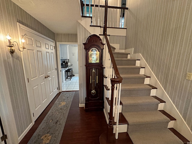 entrance foyer featuring a textured ceiling, wood finished floors, stairway, wallpapered walls, and baseboards