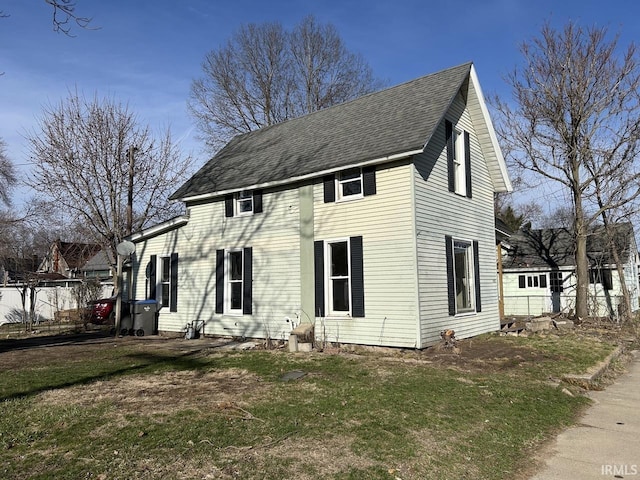 colonial house featuring roof with shingles, a front yard, and fence